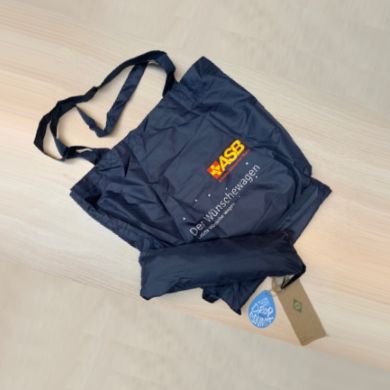 Dunkelblaue Einkaufstasche mit ASB-Logo und „Der Wünschewagen“-Aufdruck, zusammenfaltbar mit Umwelt-Label „Stop Ocean Plastic“.